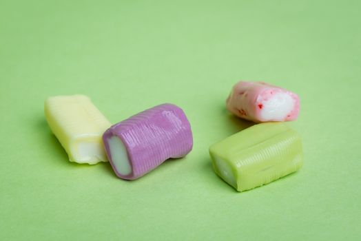 Strawberry, grape, banana and green apple chewy candies on a green background.
