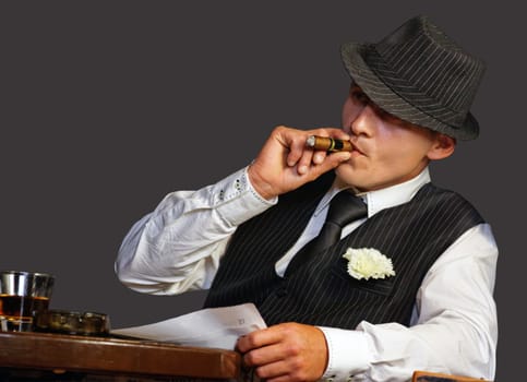 young gangster with hat smoking cigar, studio shot