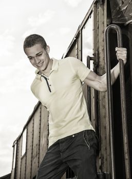 Fit guy with polo shirt hanging from old train, jumping dow while smiling