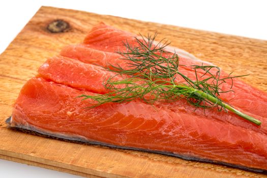 a portion of sockeye salmon prepared for grilling on a water soaked cedar wood plank with green dill