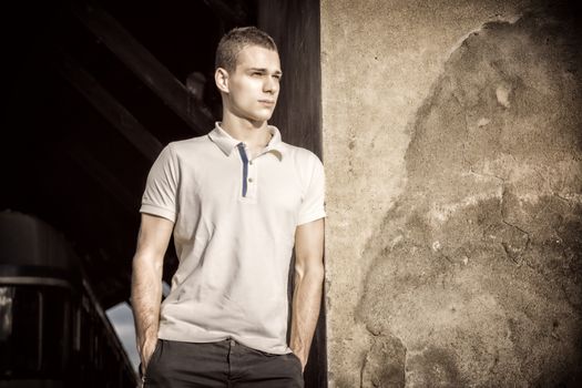 Attractive green eyed young man leaning against rough concrete wall, looking at camera