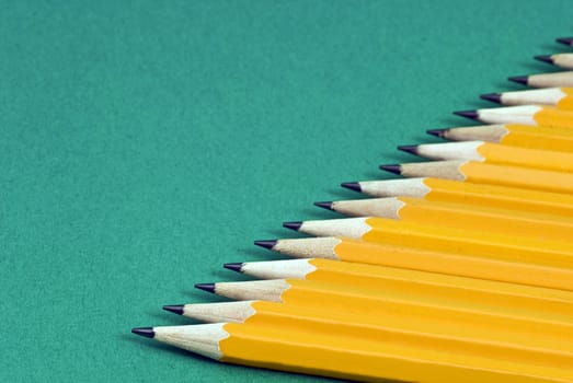 Horizontal shot of yellow sharpened pencils in a row with focus on foreground on a green background