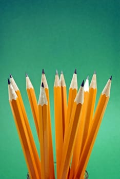 Vertical shot of a group of yellow pencils on a green background
