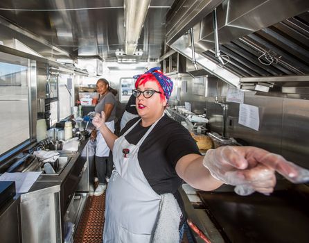 Chef with pink hair directs crew on busy food truck