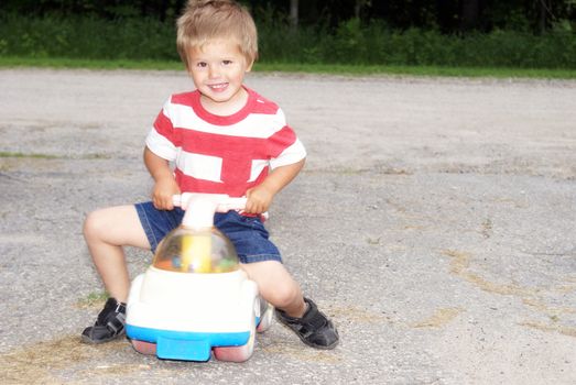 A young toddler playfully rides his toy outdoors.