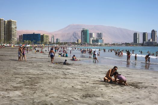IQUIQUE, CHILE - JANUARY 23, 2015: Unidentified people enjoying the water and playing in the sand on the crowded Cavancha beach on January 23, 2015 in Iquique, Chile. Iquique is a popular beach town and free port city in Northern Chile.  