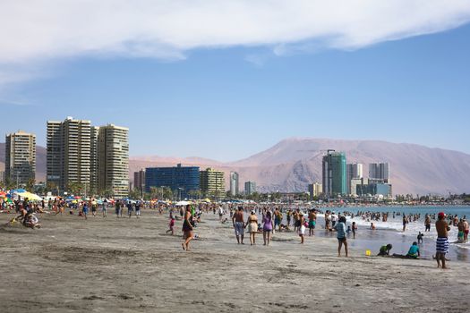 IQUIQUE, CHILE - JANUARY 23, 2015: Unidentified people enjoying the water and playing in the sand on the crowded Cavancha beach on January 23, 2015 in Iquique, Chile. Iquique is a popular beach town and free port city in Northern Chile.  