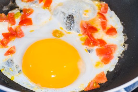 Preparation breakfast. Fried eggs with peppers and tomatoes in a pan.