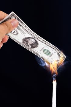 View of one hundred dollar banknote burning with a match stick, on black background.