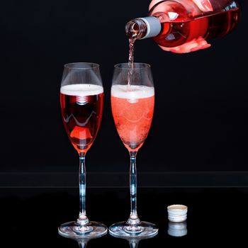Female hand pours red sparkling wine in glasses