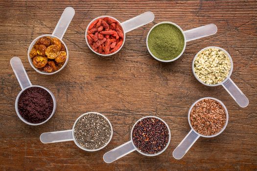 superfood abstract (wheatgrass, acai berry, goji berry, flax seed,chia seed,goldenberry,hemp seed, quinoa grain) - top view of measuring scoops surrounding  a copy space on a rustic wood