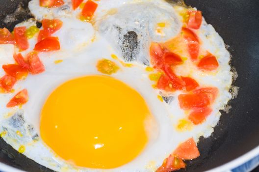 Preparation breakfast. Fried eggs with peppers and tomatoes in a pan.