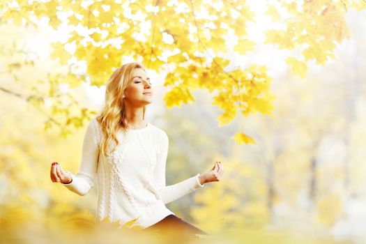 Beautiful young woman sitting in autumn park in lotus yoga position