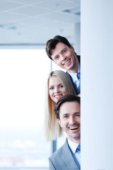 Happy business people looking out from corner in office