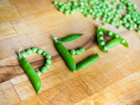 Word PEA created with peas on a wooden board with a podded peas in the background
