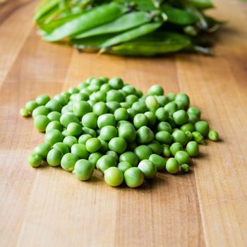 Pile of podded peas on wooden board with pods in the background