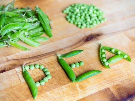 Word PEA created with peas on a wooden board with peas and pods in the background