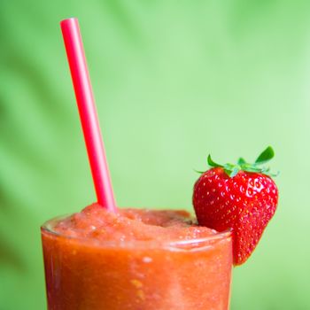 Strawberry smoothie in glass with straw and strawberry with a green background