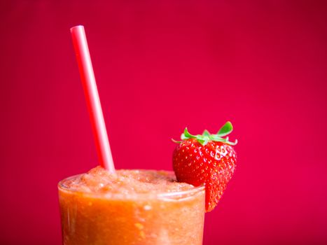 Strawberry smoothie in glass with straw and strawberry with a pink background