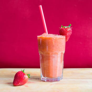 Strawberry smoothie in glass with straw and strawberry with a pink background