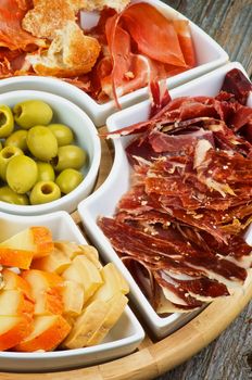 Arrangement of Spanish Snacks with Various Cheeses, Jamon, Cured Ham and Green Olives on Serving Plate closeup on Wooden background