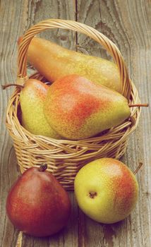 Arrangement of Red, Yellow and Conference Pears in Wicker Basket closeup on Rustic Wooden background. Retro Styled