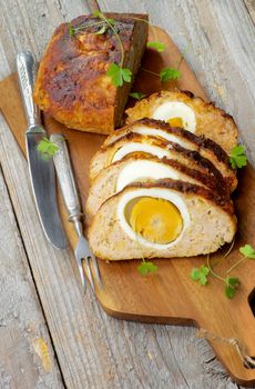 Tasty Meatloaf Stuffed with Boiled Eggs on Cutting Board with Knife and Fork closeup on Rustic Wooden background