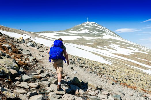 Hiker with big traveling rucksack looking forward on the mountain trail, adventure travel and discovery