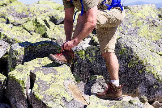 Hiker with big traveling rucksack tying up laces on the mountain trail, adventure travel and discovery