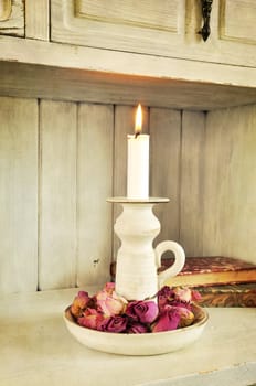 Softly textured image of candle with dried roses and books. Vintage style.