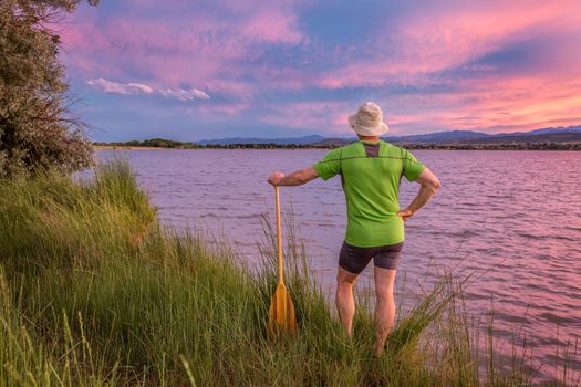 male canoe paddler watching pink sunset sky over a lake and Front Range of Rocky Mountains