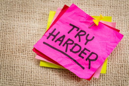 try harder - motivation words on a  purple sticky note against burlap canvas