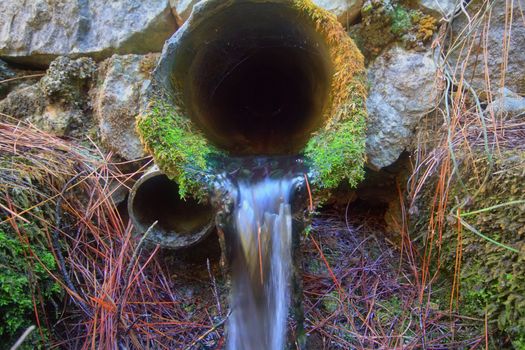 Two pipes laid under the road for water drainage. One mossy pipe flowing clean water.