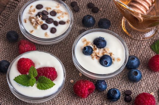 Three Little Bowls Full of Healthy Yogurt with Fruit or Chocolate and Honey on Wooden Rustic Table