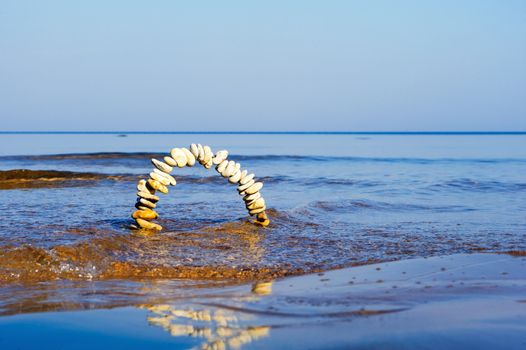 Arch of pebbles in the blue waves