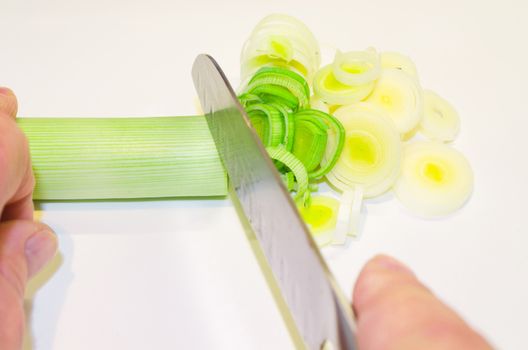 Hand of the cook, while cutting vegetables on a wooden board.