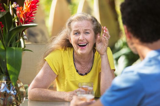 Amazed mature woman at table with friend on vacation