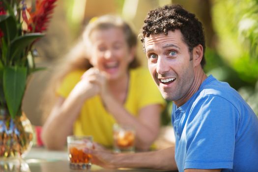 Laughing man in blue having drinks with woman outdoors