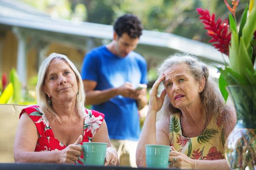 Mature female friends annoyed with man texting on phone