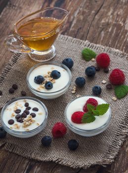 Three Little Bowls Full of Healthy Yogurt with Fruit or Chocolate and Honey on Wooden Rustic Table