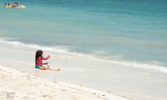 Trinidad, Cuba - July 2, 2012: Child sitting playing on tropical white sand beach at waters edge in Brisas Trinidad del Mar, Cuba.