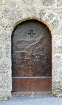 Old studded metal door, decorated with a cross and engraving, in a stone wall in Salzburg, Austria