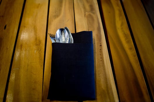 fork and spoon in dark blue cloth,on wooden table background