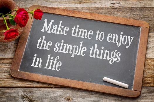 Make time to enjoy the simple things   inspirational advice - white chalk text on a vintage slate blackboard with red roses against rustic wood