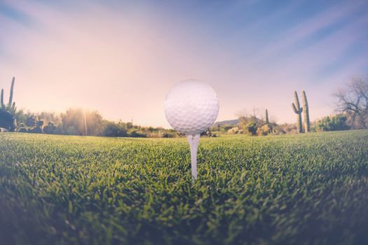 Super wide angle view of golf ball on tee with desert fairway and stunning Arizona sunset in background