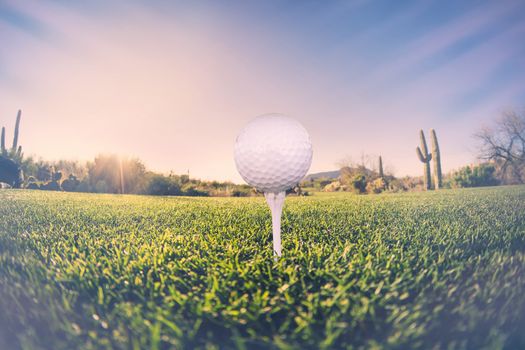 Super wide angle view of golf ball on tee with desert fairway and stunning Arizona sunset in background