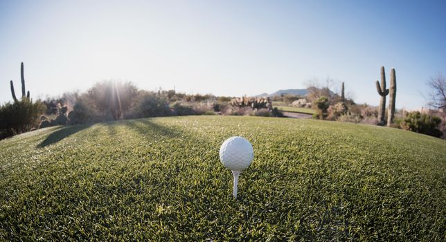 Super wide angle view of golf ball on tee with desert fairway and stunning Arizona sunset in background