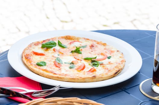 Pizza on a simple blue table outside a pizzeria.