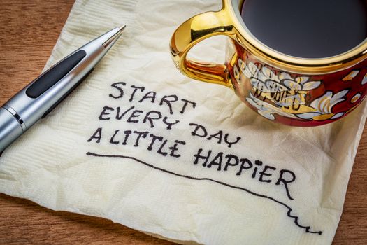 Start every day a little happier - happiness and attitude concept - handwriting on a napkin with cup of coffee