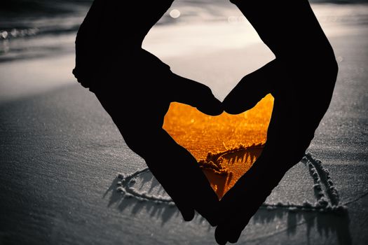 Close up of hands forming heart against one heart drawn in the sand 